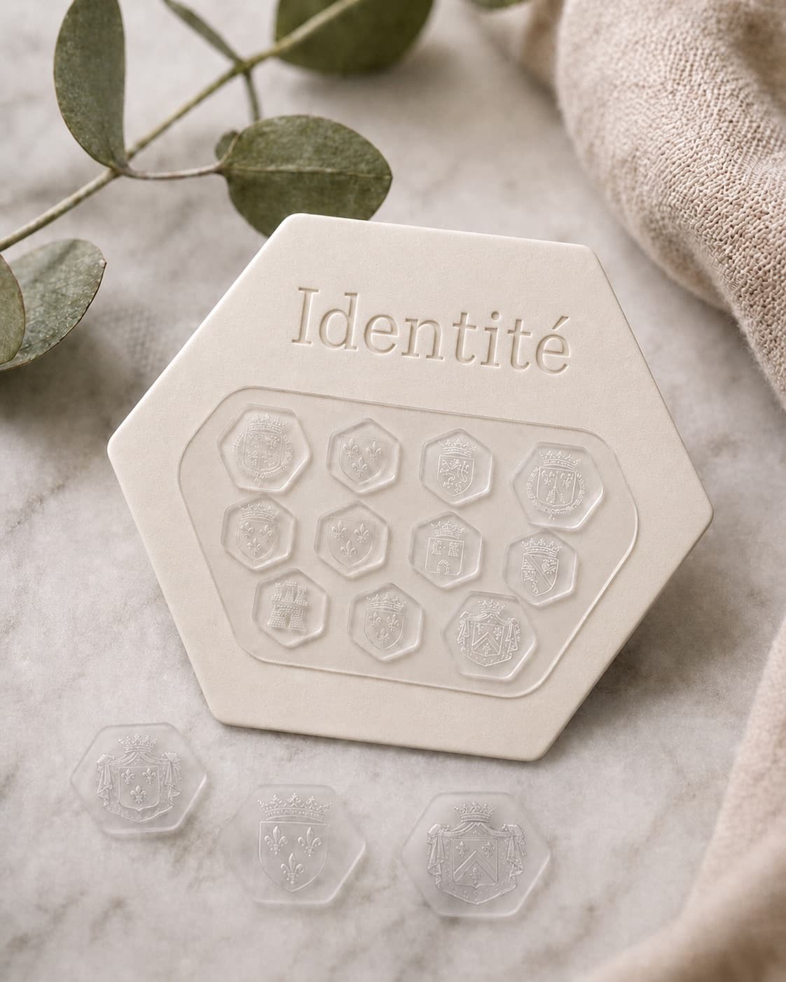 Ten Identité hexagonal glass crests arranged on a presentation plate, each embossed with a different French royal house coat of arms