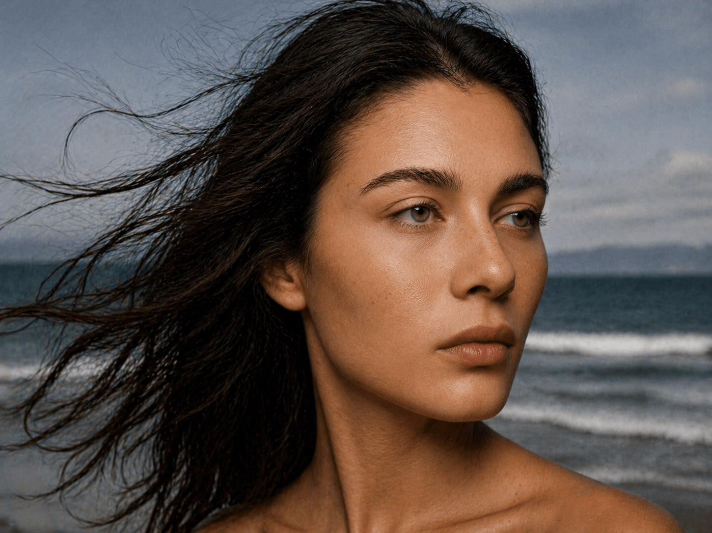 A close-up portrait of a woman on a beach, hair flowing in the wind